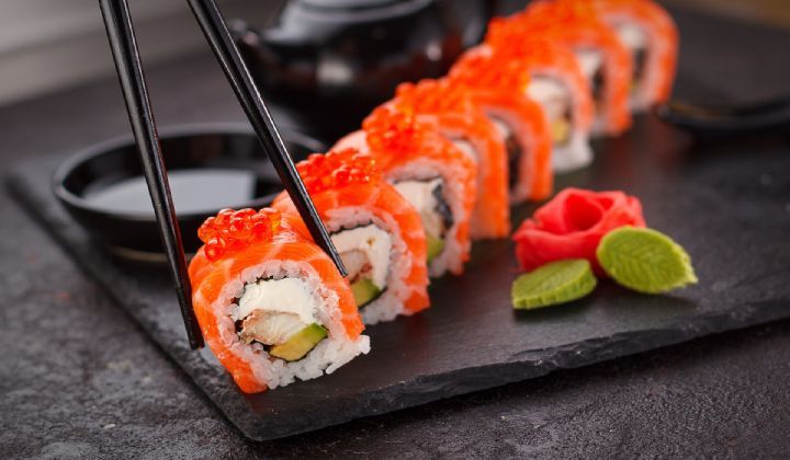 A close up of a person eating sushi with chopsticks.