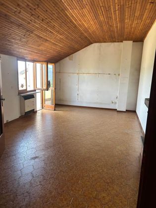 Stanza vuota con pavimento in sughero, soffitto inclinato rivestito in legno, pareti bianche e una porta-finestra aperta