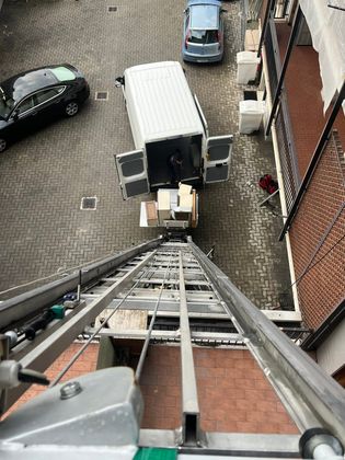 Vista dall’alto di una scala su un furgone bianco per le consegne, in un vicolo acciottolato con auto parcheggiate ed edifici