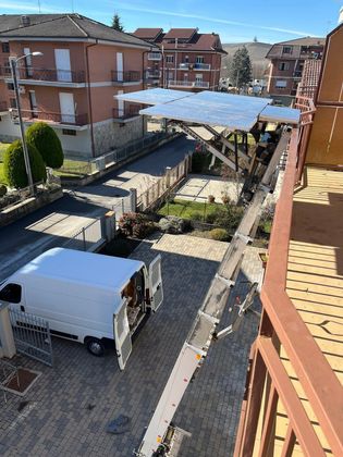 Cortile soleggiato tra palazzi rossi, con una tenda bianca e un veicolo parcheggiato sotto.