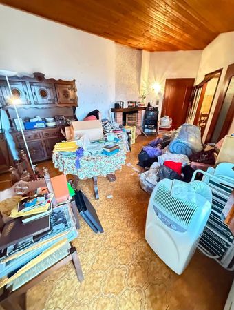 Soggiorno disordinato con sedie, tavolo, mobili e soffitto in legno, illuminato da una calda luce interna