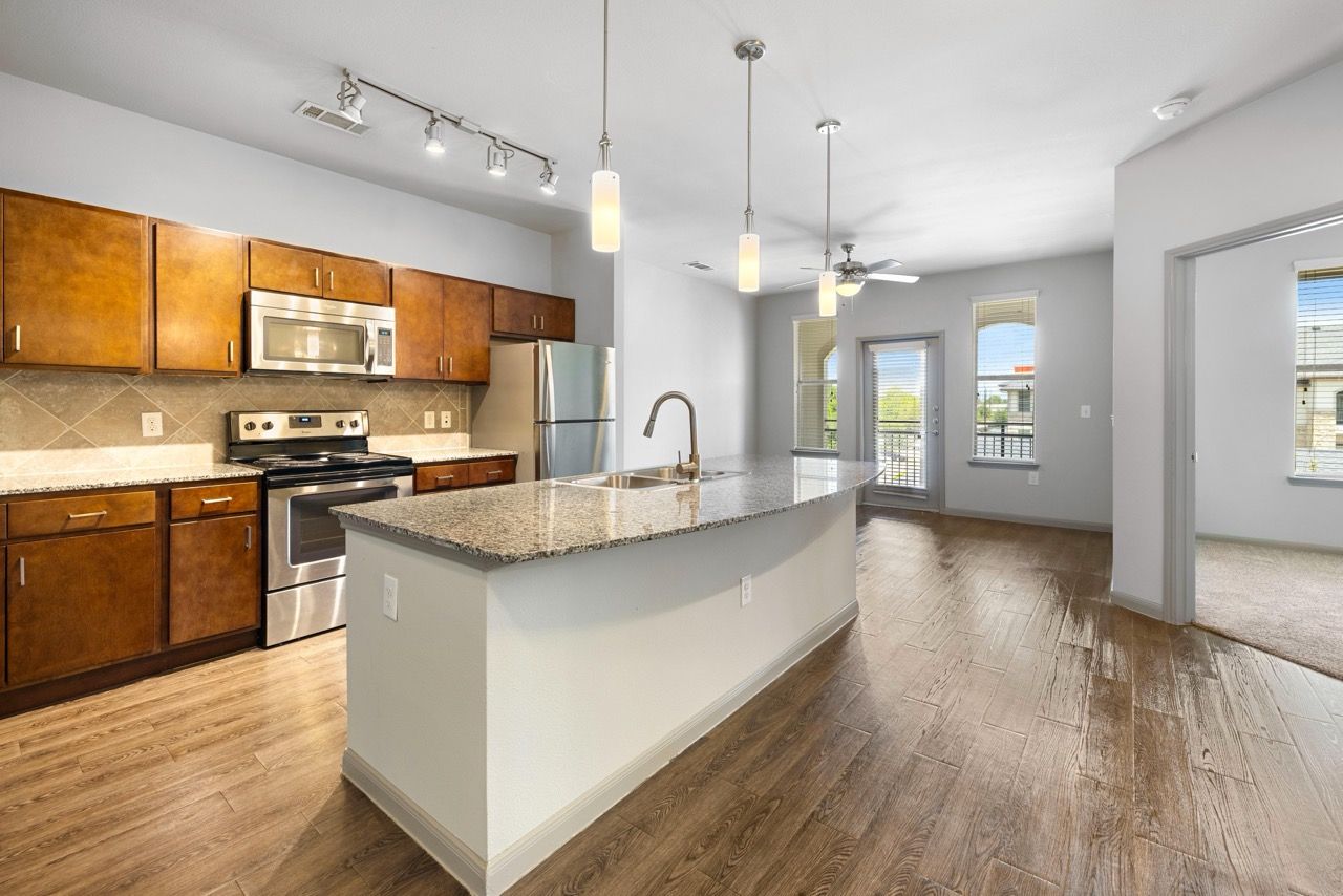 Open-concept kitchen with island, granite countertops, and stainless-steel appliances at Olympus at Waterside Estates, offering apartments in Richmond, TX.