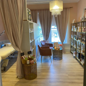 Cozy spa-style room with beige curtains, gold accents, shelves, chairs, and a crystal chandelier.
