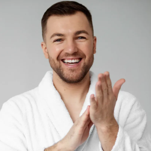 Smiling person in a white robe clapping hands against a gray background