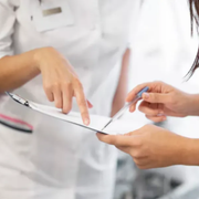 Two clinicians in white coats reviewing a clipboard and pointing at a document