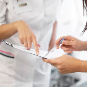Two clinicians in white coats reviewing a clipboard and pointing at a document