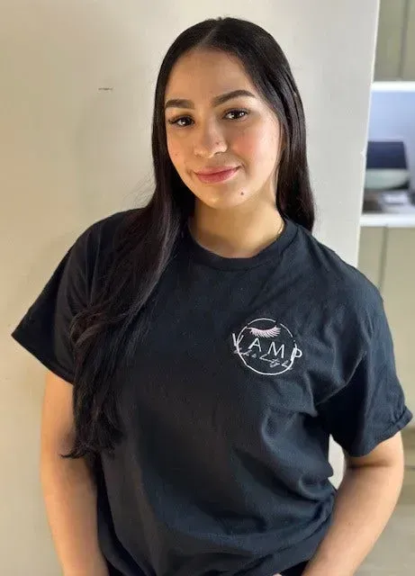 Person standing indoors in a black T-shirt with a logo, smiling at the camera.