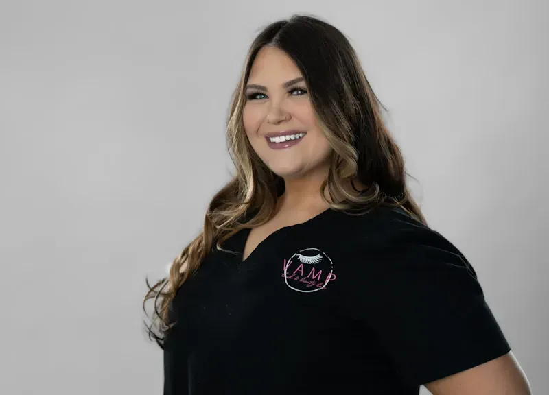 Smiling woman in a black shirt with a logo, standing against a light gray background