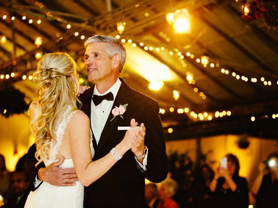 Father and Daughter Dance A bride and a man in a tuxedo dancing in a warmly lit, string-light-decorated venue.