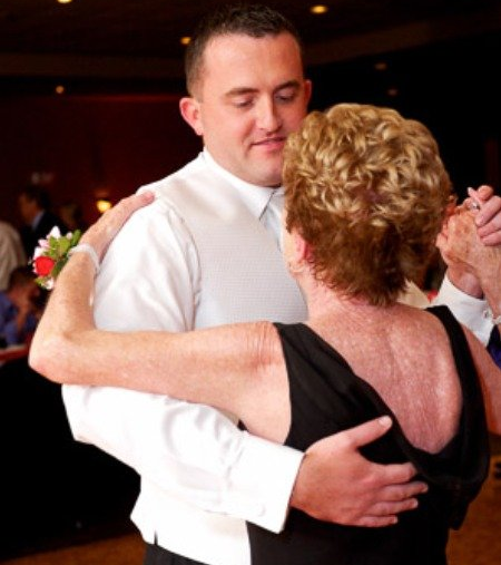Mother and Son dance A person in a white dress shirt and vest dancing with a partner wearing a black dress in a dimly lit indoor setting.
