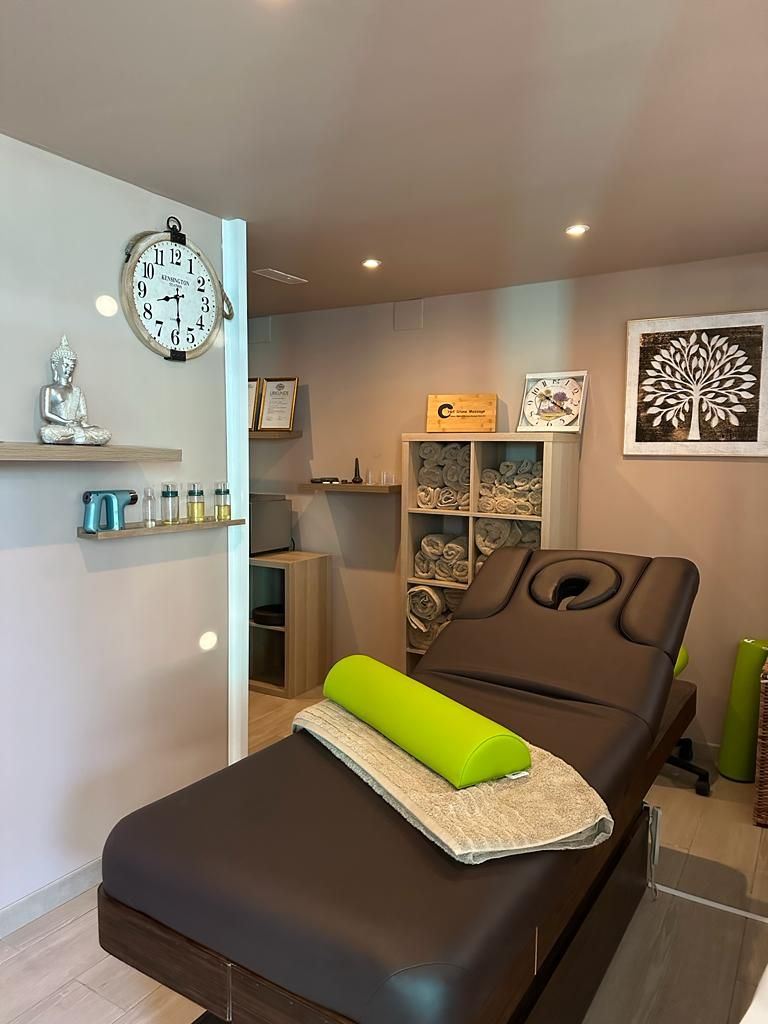 Massage chair in a spa room with shelves, wall clock, and framed art.