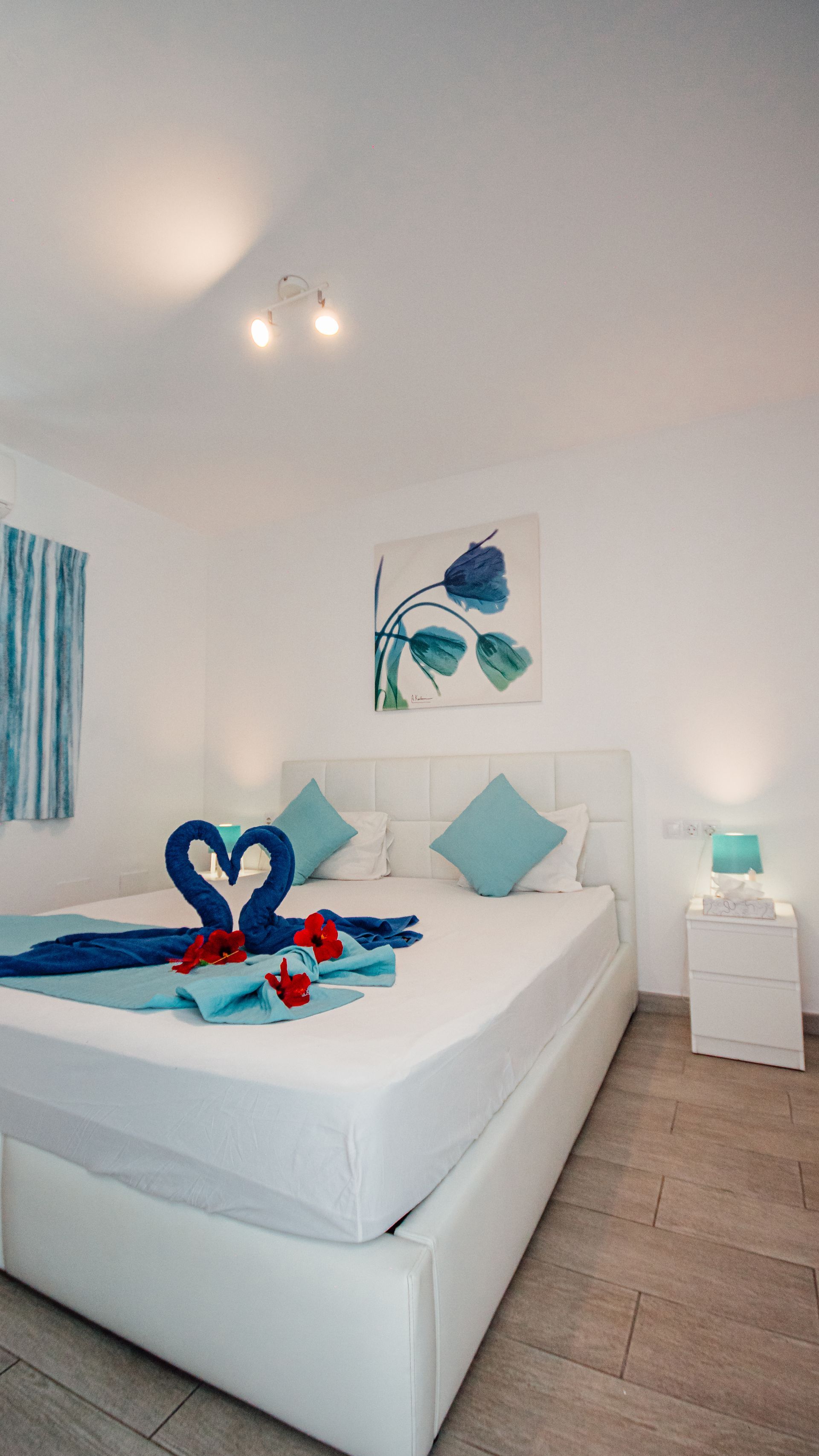 White hotel bedroom with a neatly made bed, blue decor, and towel swan arrangement on the bed.