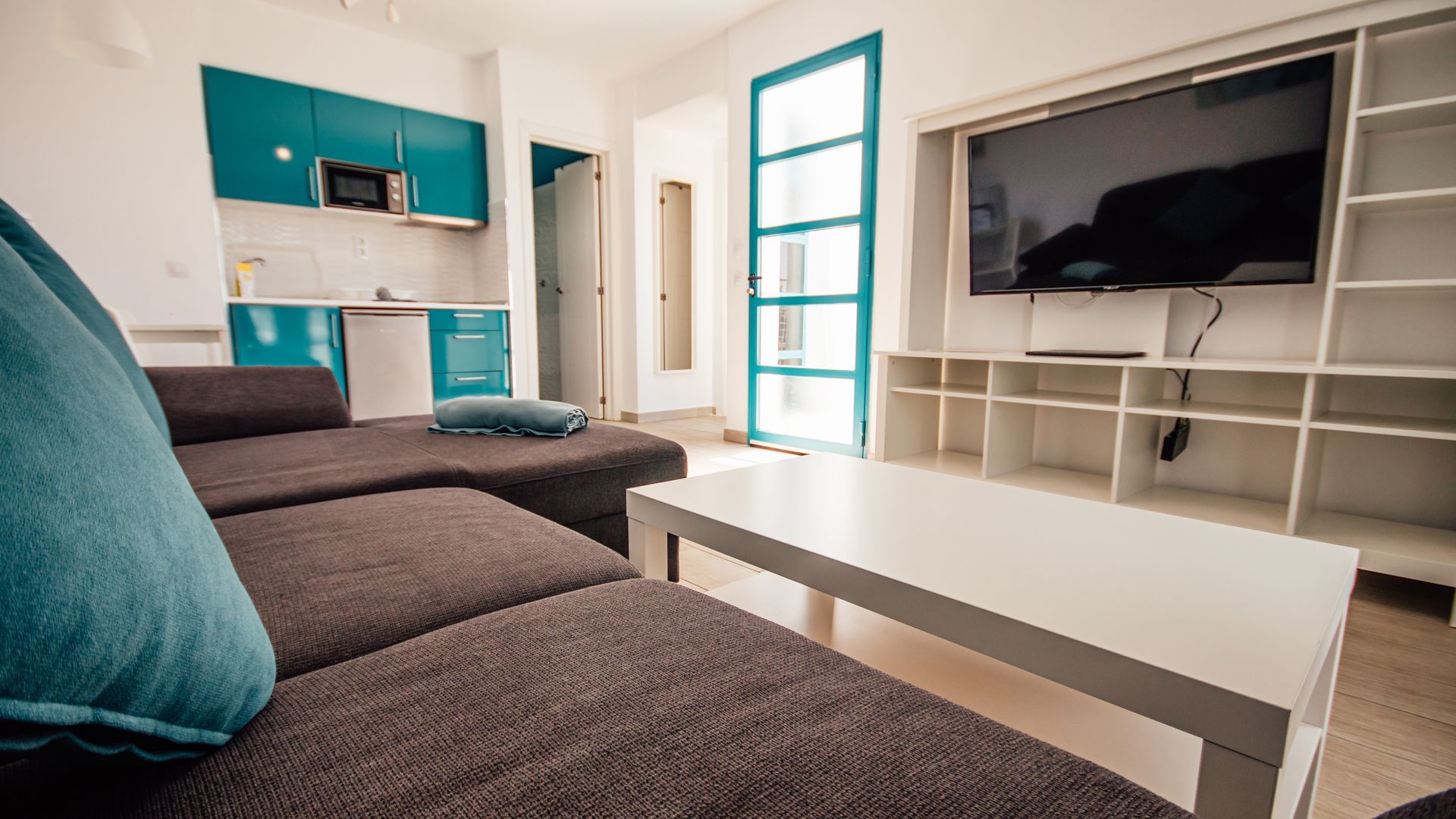 Modern living room with gray sectional sofa, white coffee table, wall-mounted TV, and teal accents