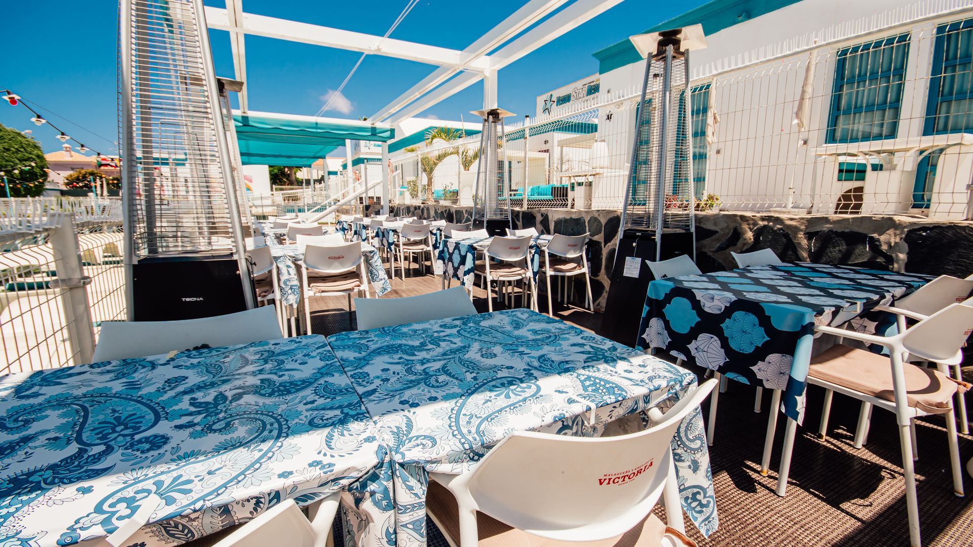 Outdoor café terrace with blue-and-white tables, chairs, and a sunny waterfront view
