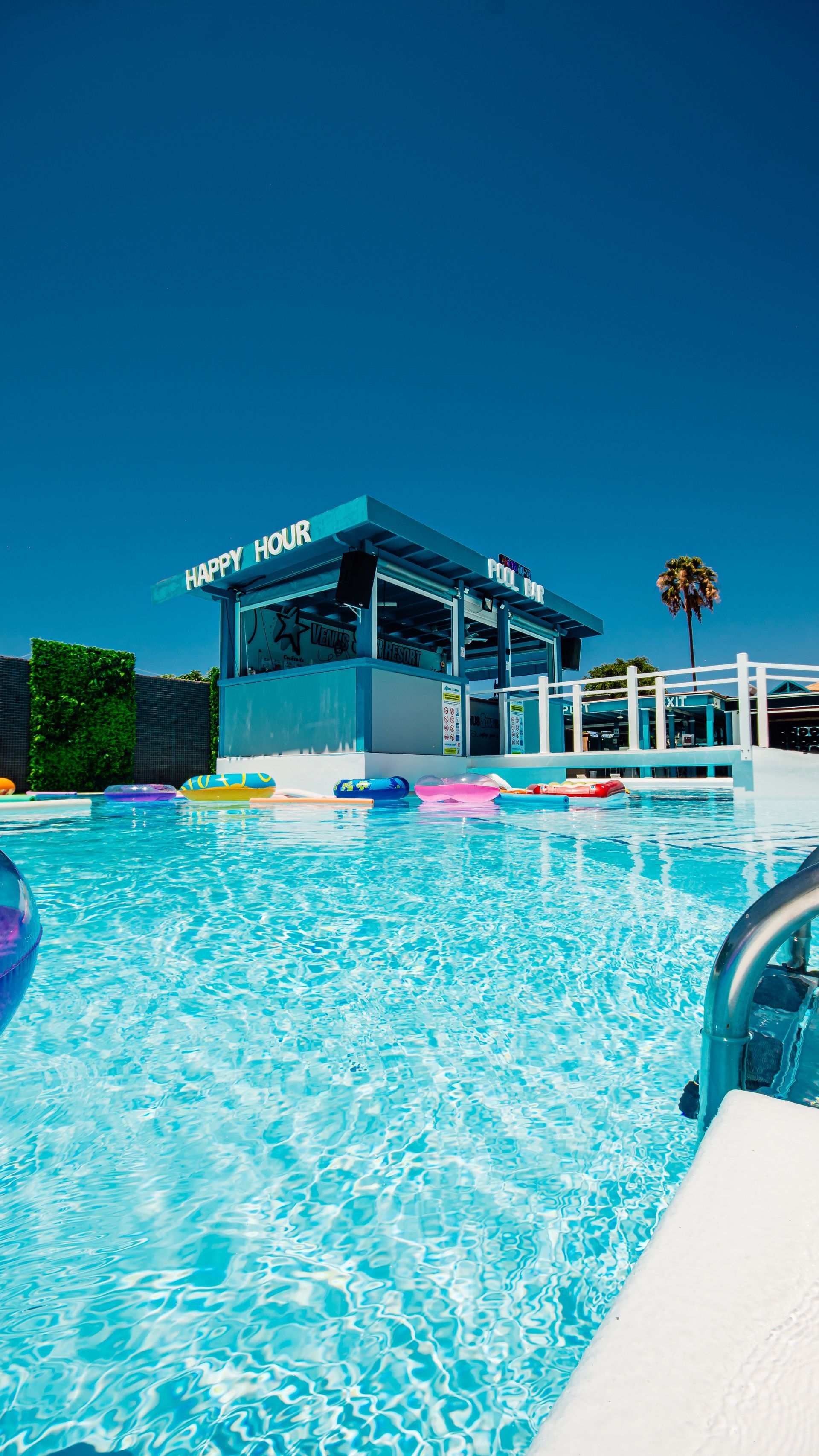 Bright turquoise swimming pool beside a modern open-air bar under a clear blue sky.