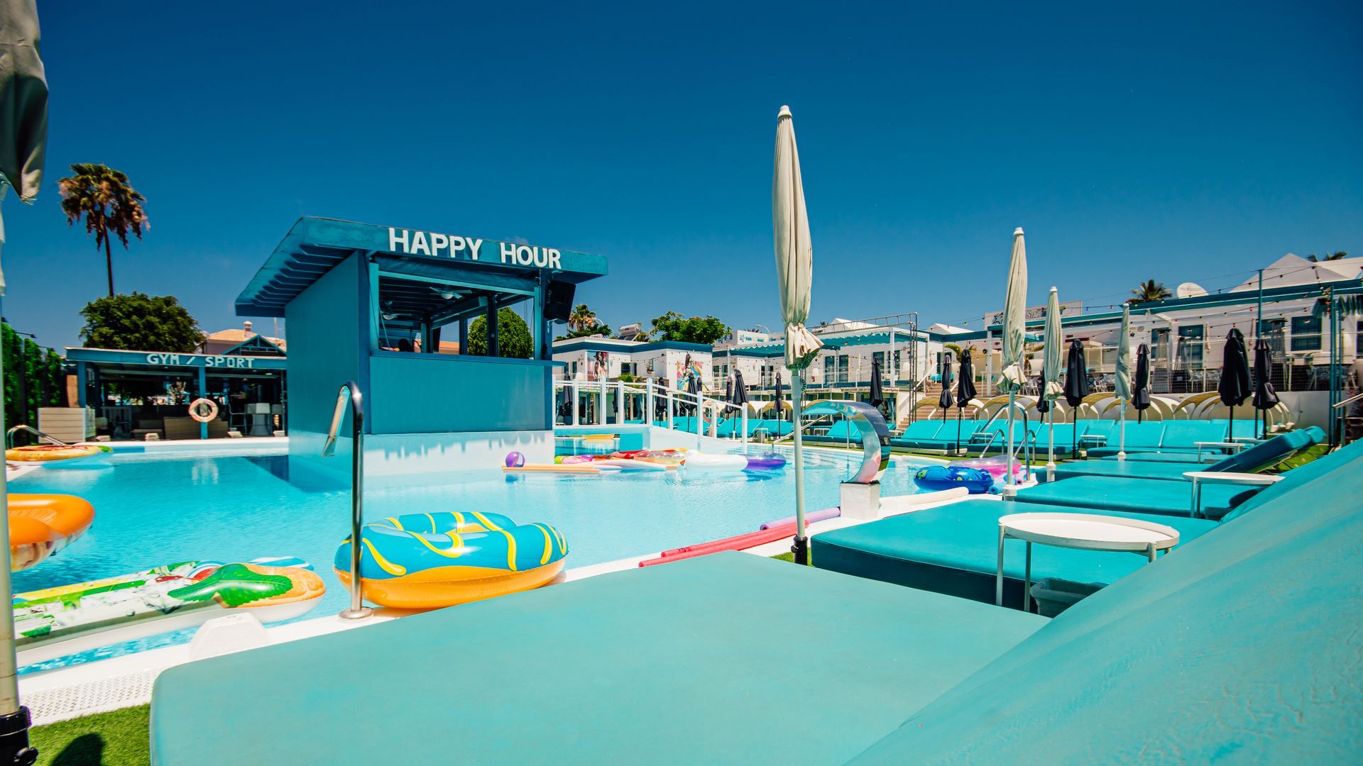 Outdoor water park with turquoise pools, colorful slides, and sun umbrellas under a clear blue sky