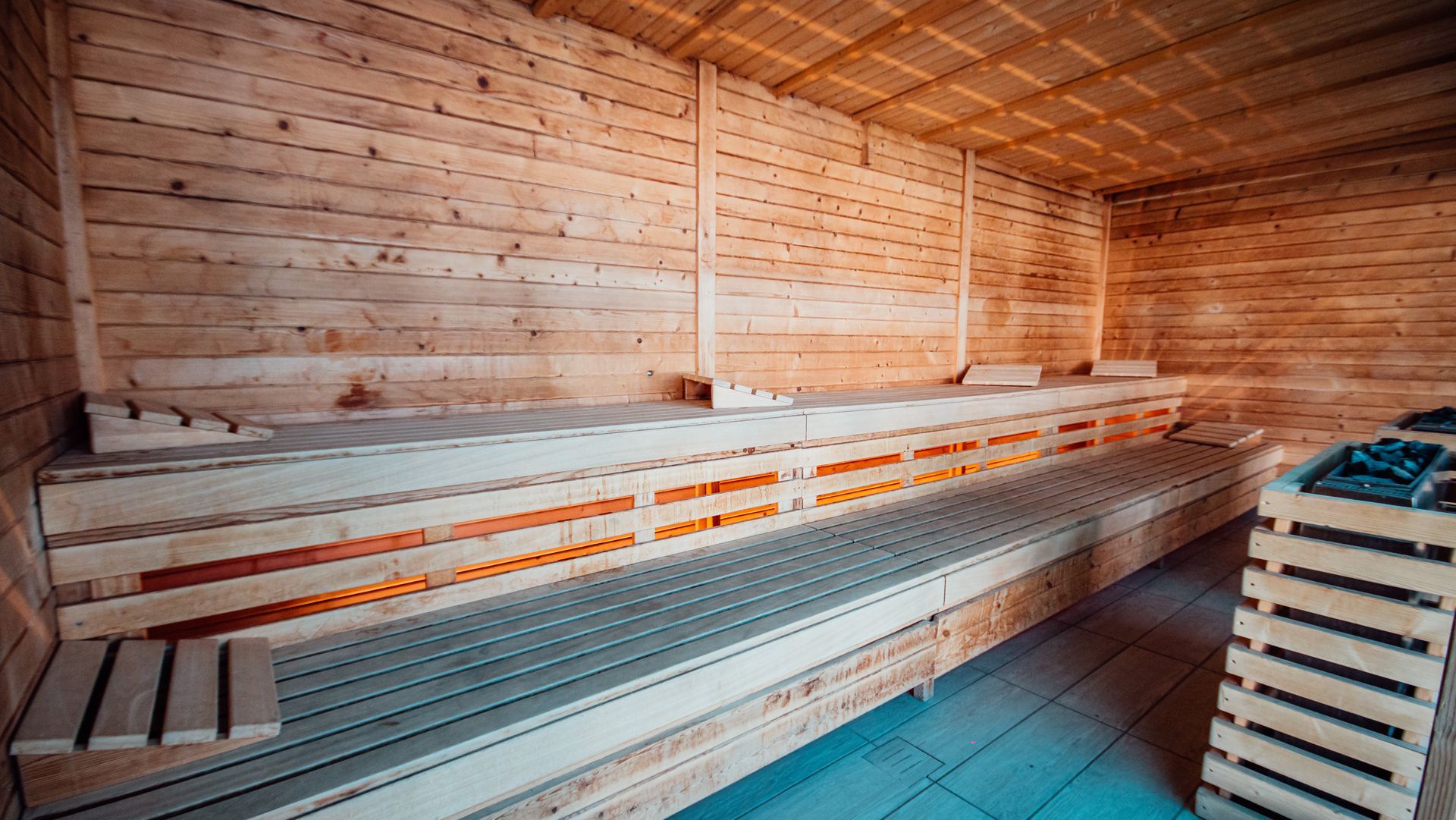 Wood-paneled sauna with tiered wooden benches and floor mats, warmly lit interior.
