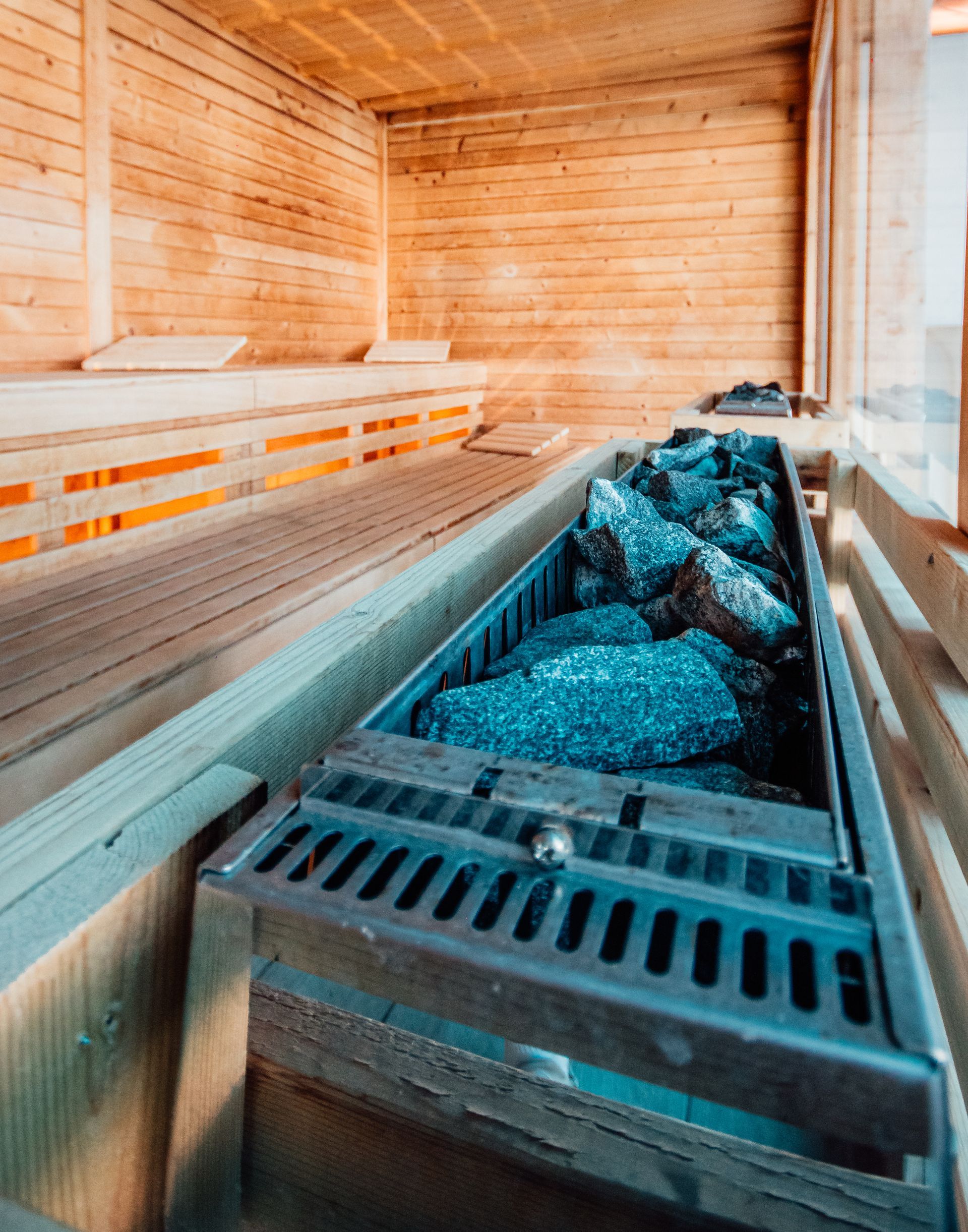 Wood-paneled sauna with wooden benches and a metal stove filled with hot stones