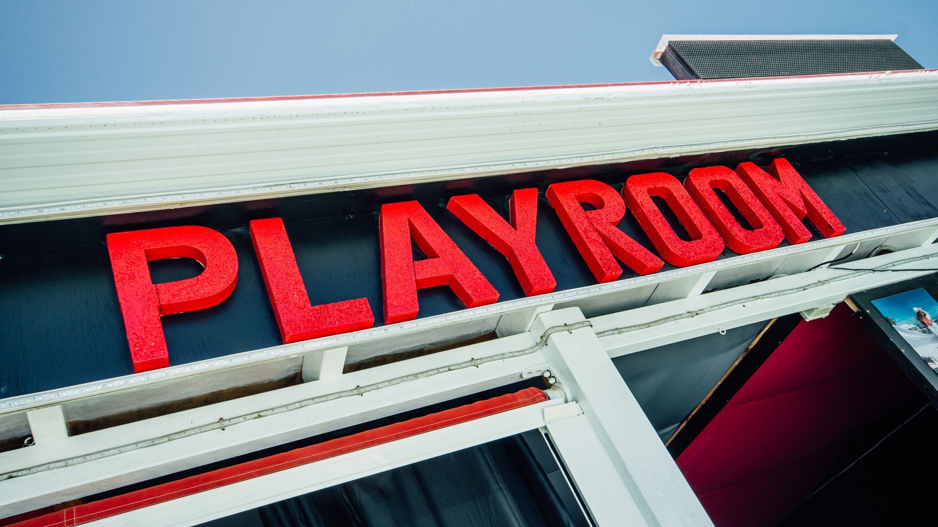 Red PLAYROOM sign mounted on a building exterior under a blue sky