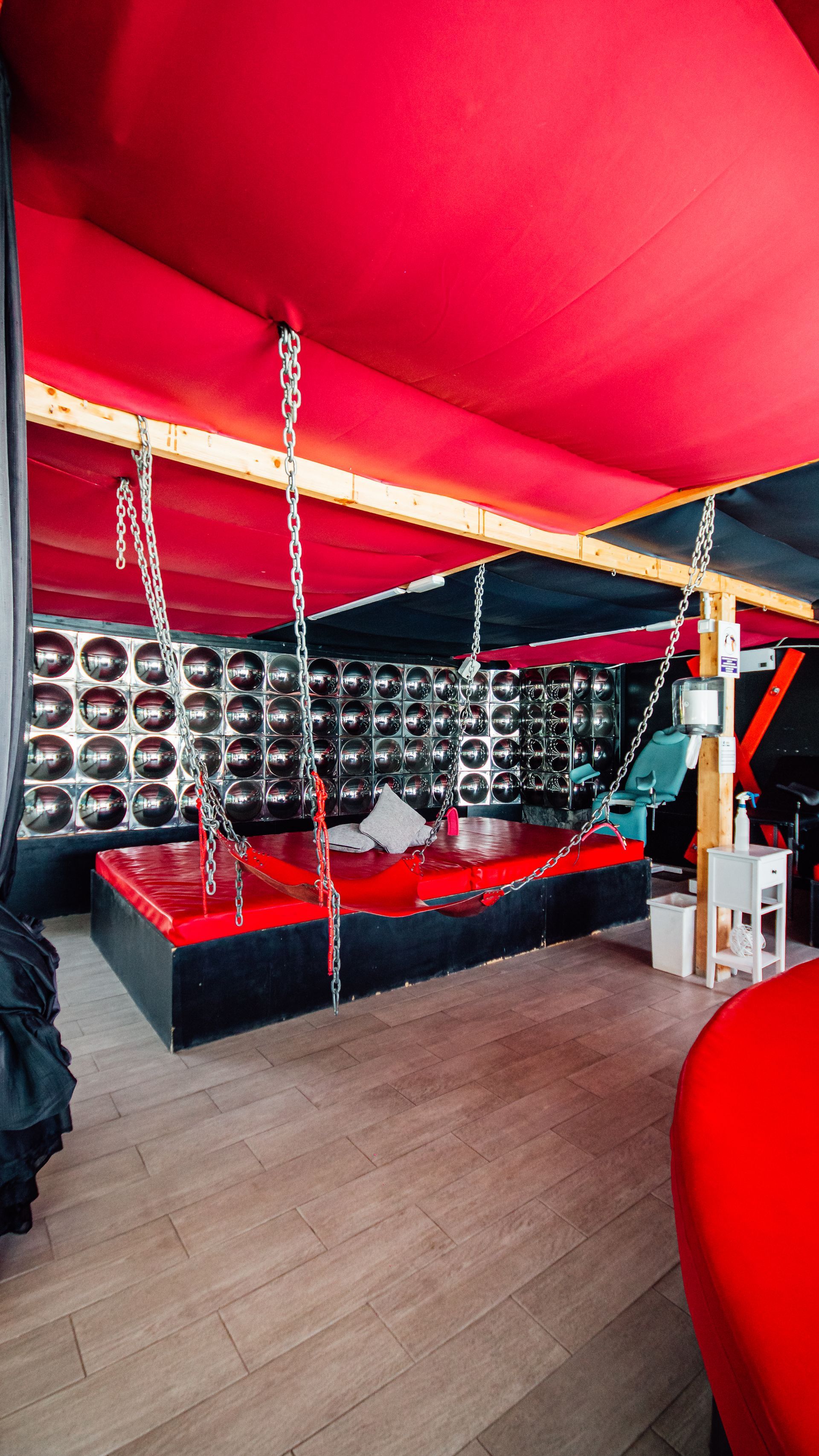 Red-canopy lounge with black-and-red seating, patterned wall, and a hanging swing chair on wood flooring