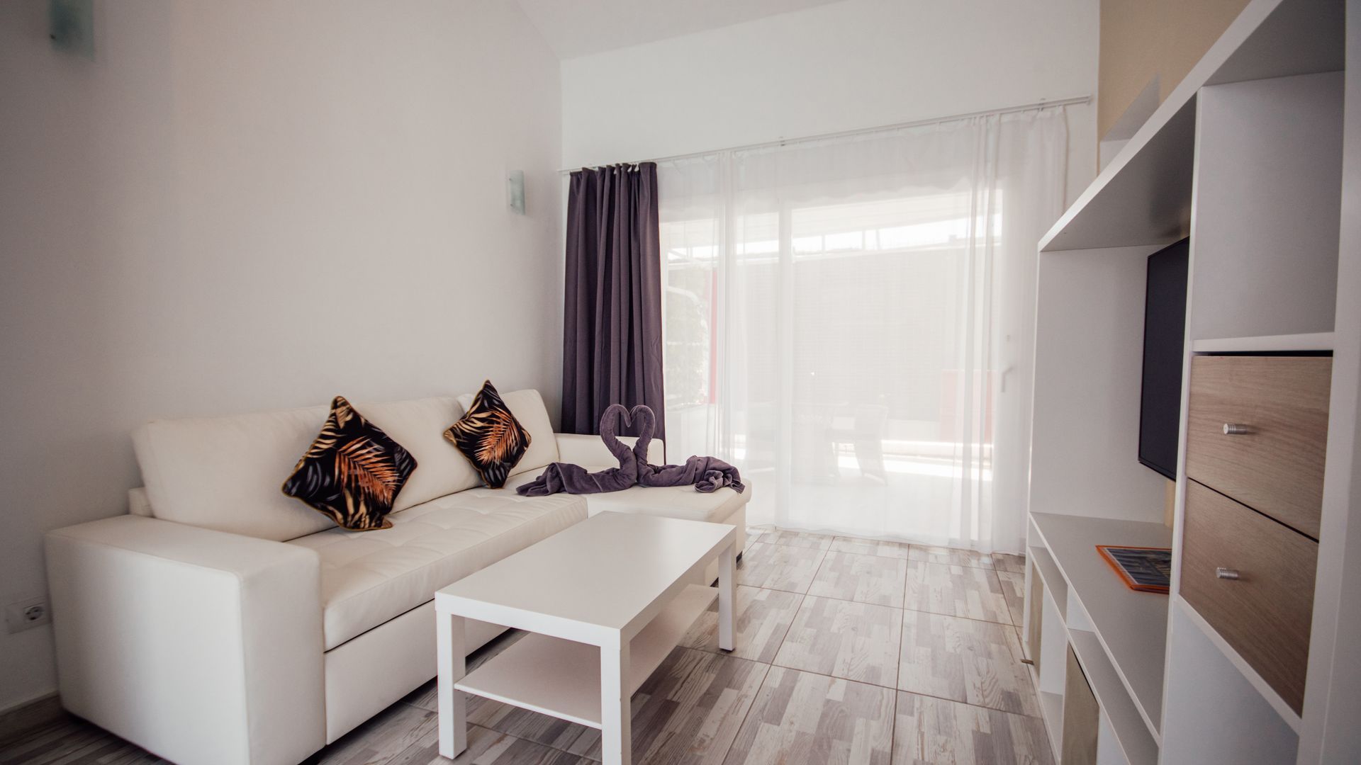 Bright living room with white sofa, coffee table, curtains, and built-in shelving.