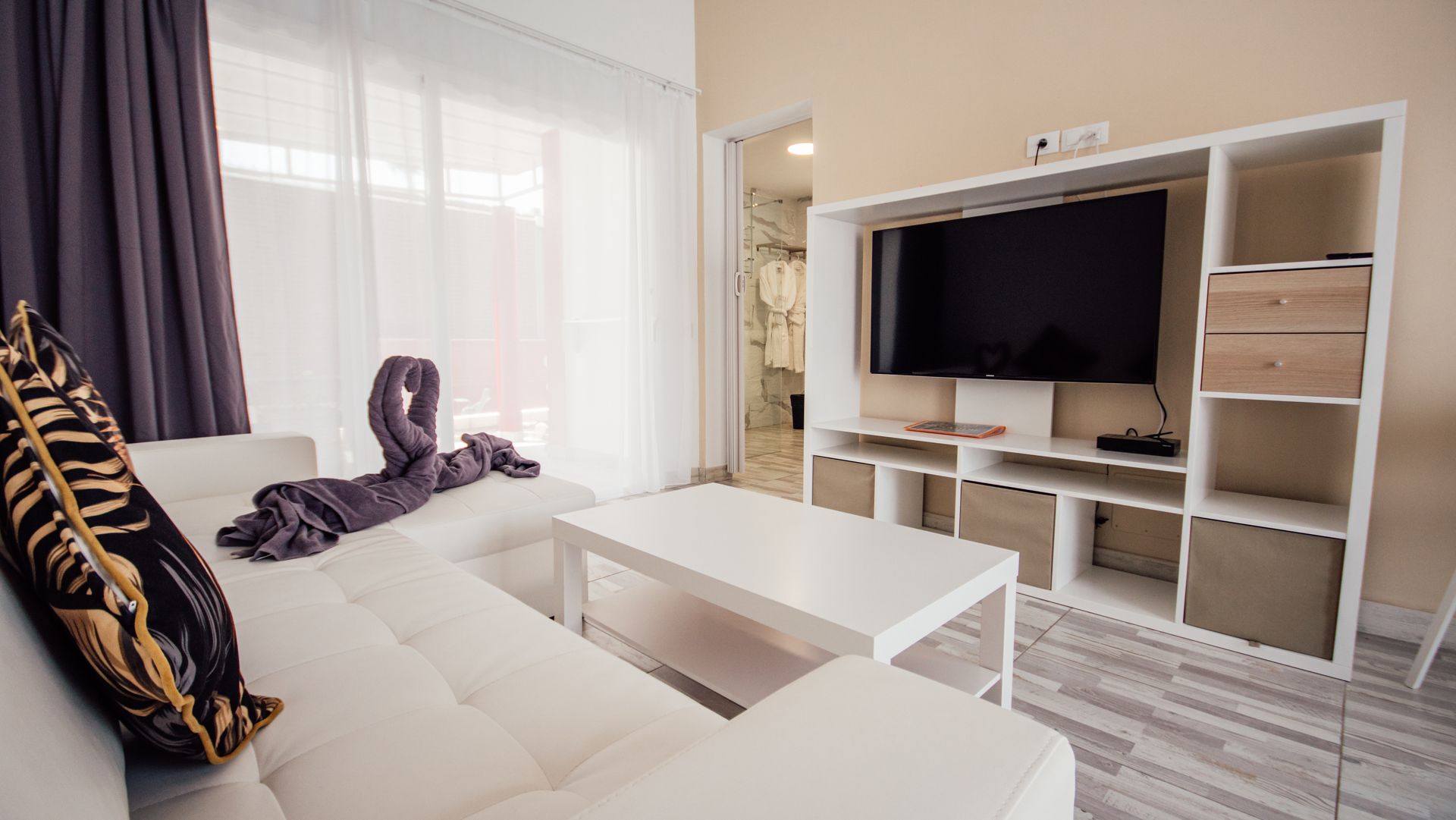 Bright modern living room with white sofa, coffee table, TV unit, and large window curtains