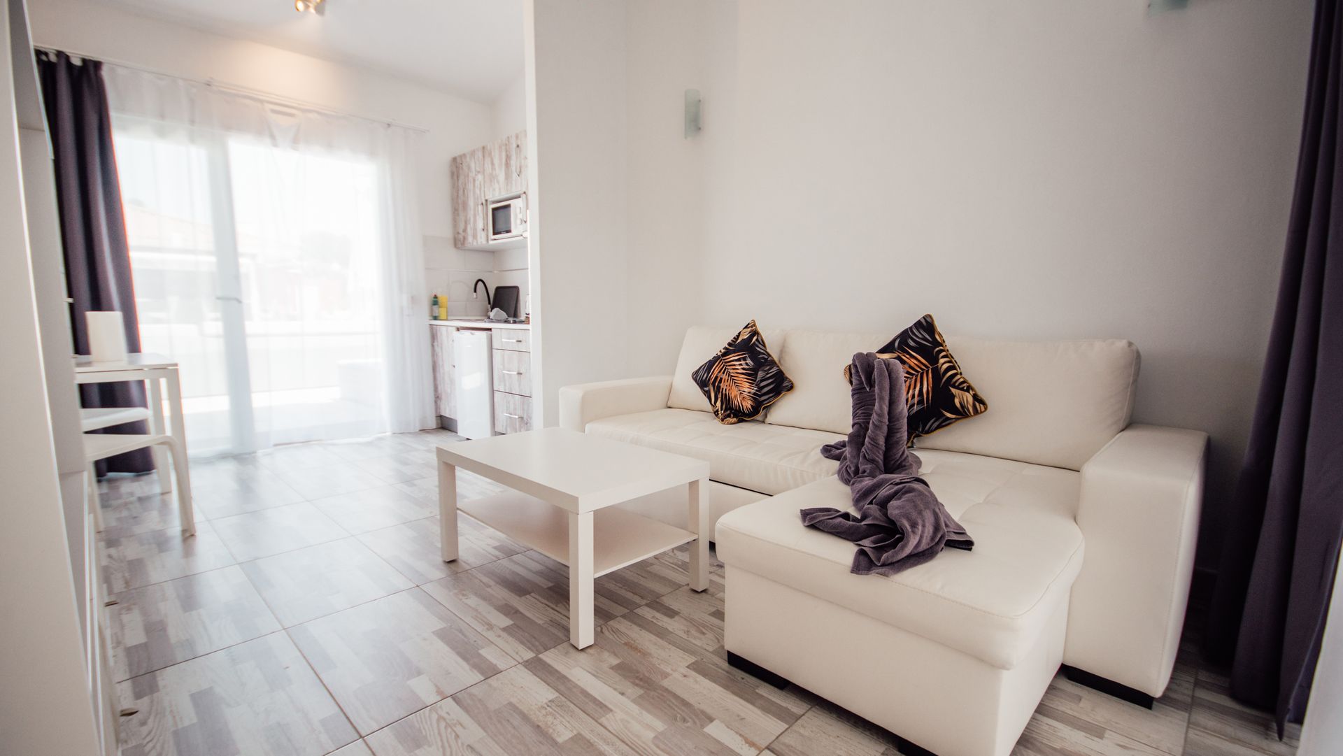 Bright modern living room with white sofa, coffee table, sheer curtains, and gray flooring