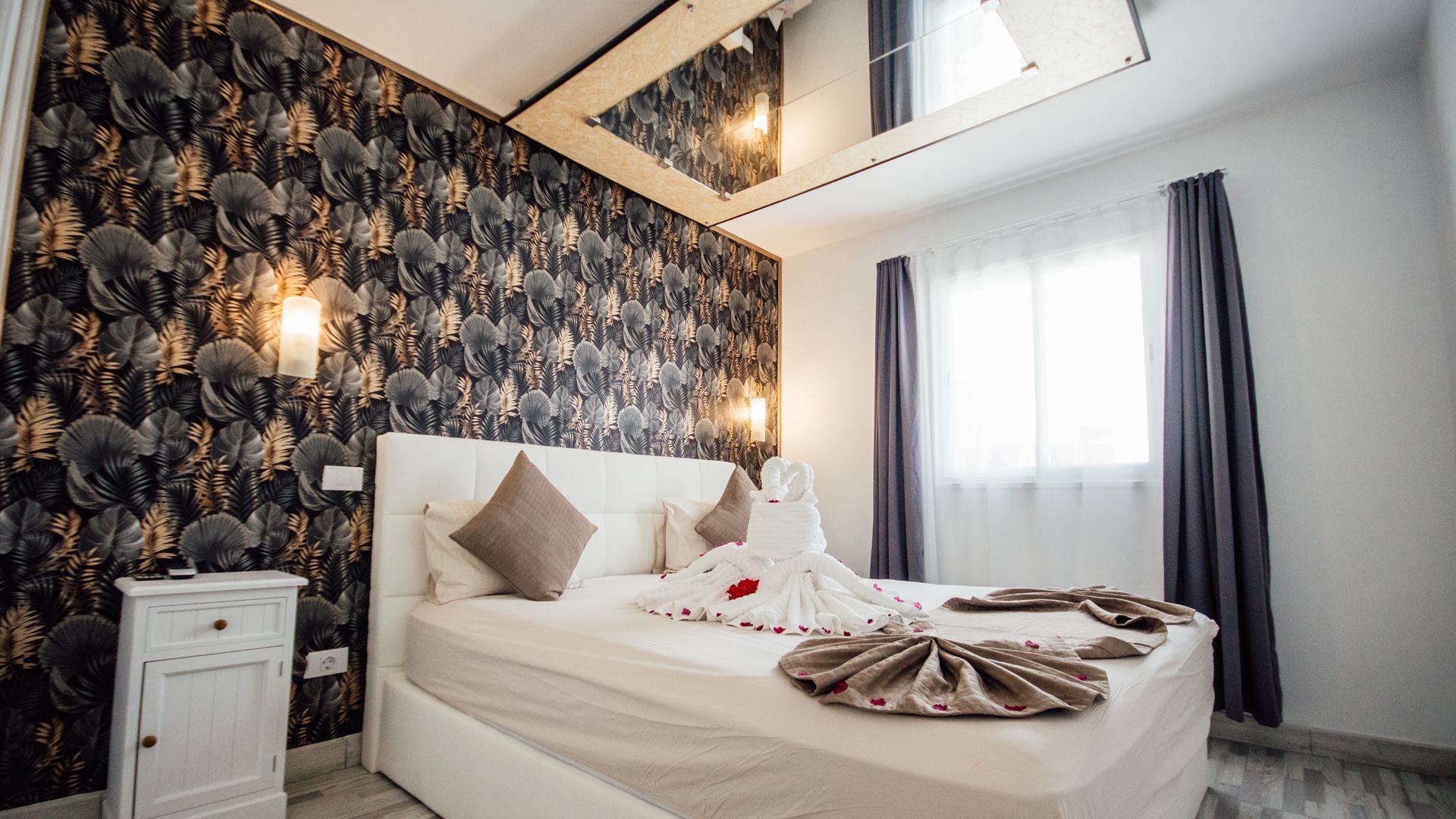 Cozy bedroom with floral wallpaper, white bed, bedside lamps, and a window with dark curtains