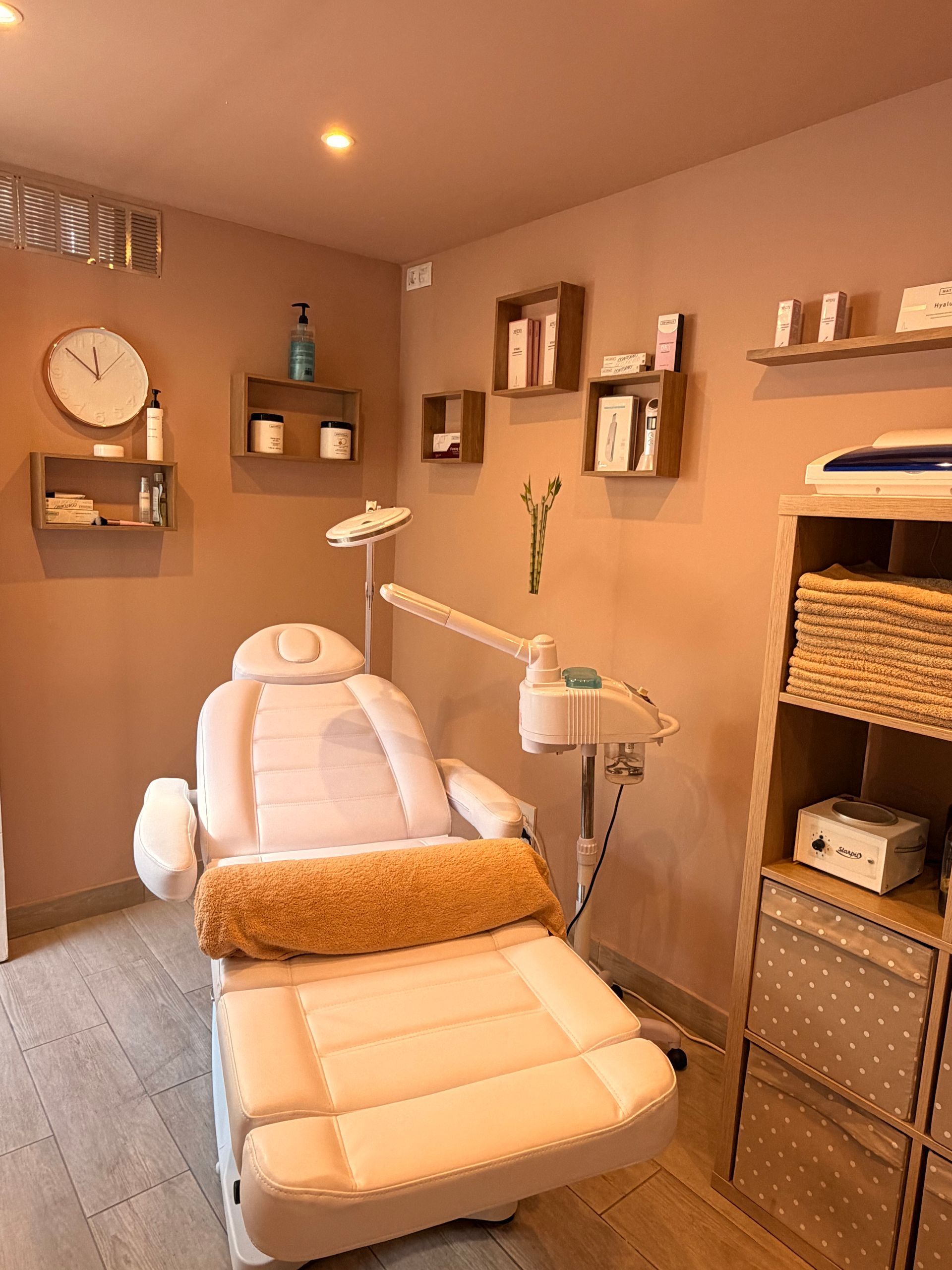 Spa treatment room with a white reclining facial chair, shelves, and warm lighting