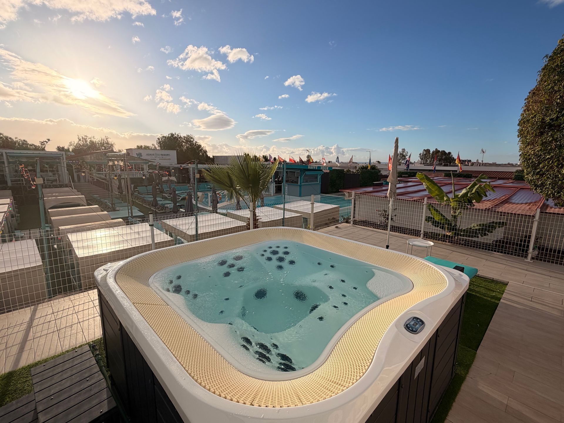 Outdoor rooftop hot tub with light blue water, sunset sky, and poolside lounge chairs