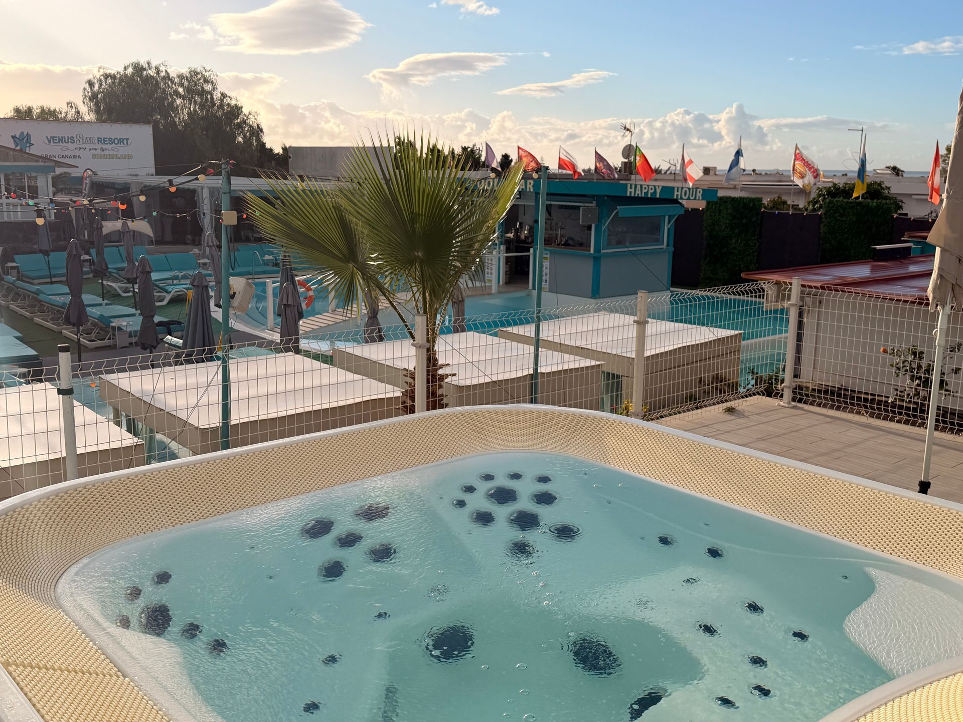 Rooftop pool with turquoise water overlooking a beachside resort and flags at sunset