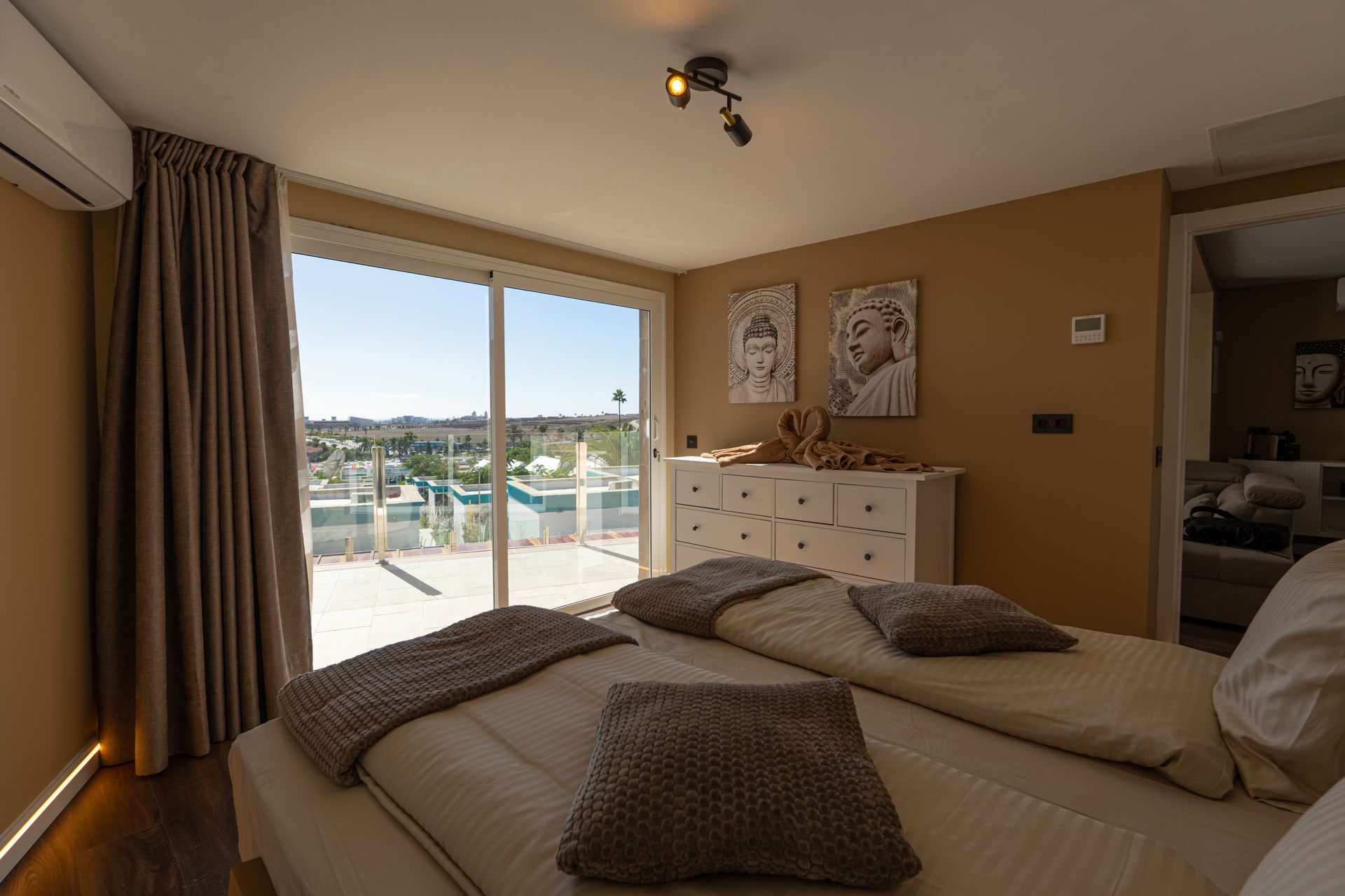 Bright bedroom with twin beds, dresser, and balcony doors overlooking a sunny pool and ocean view