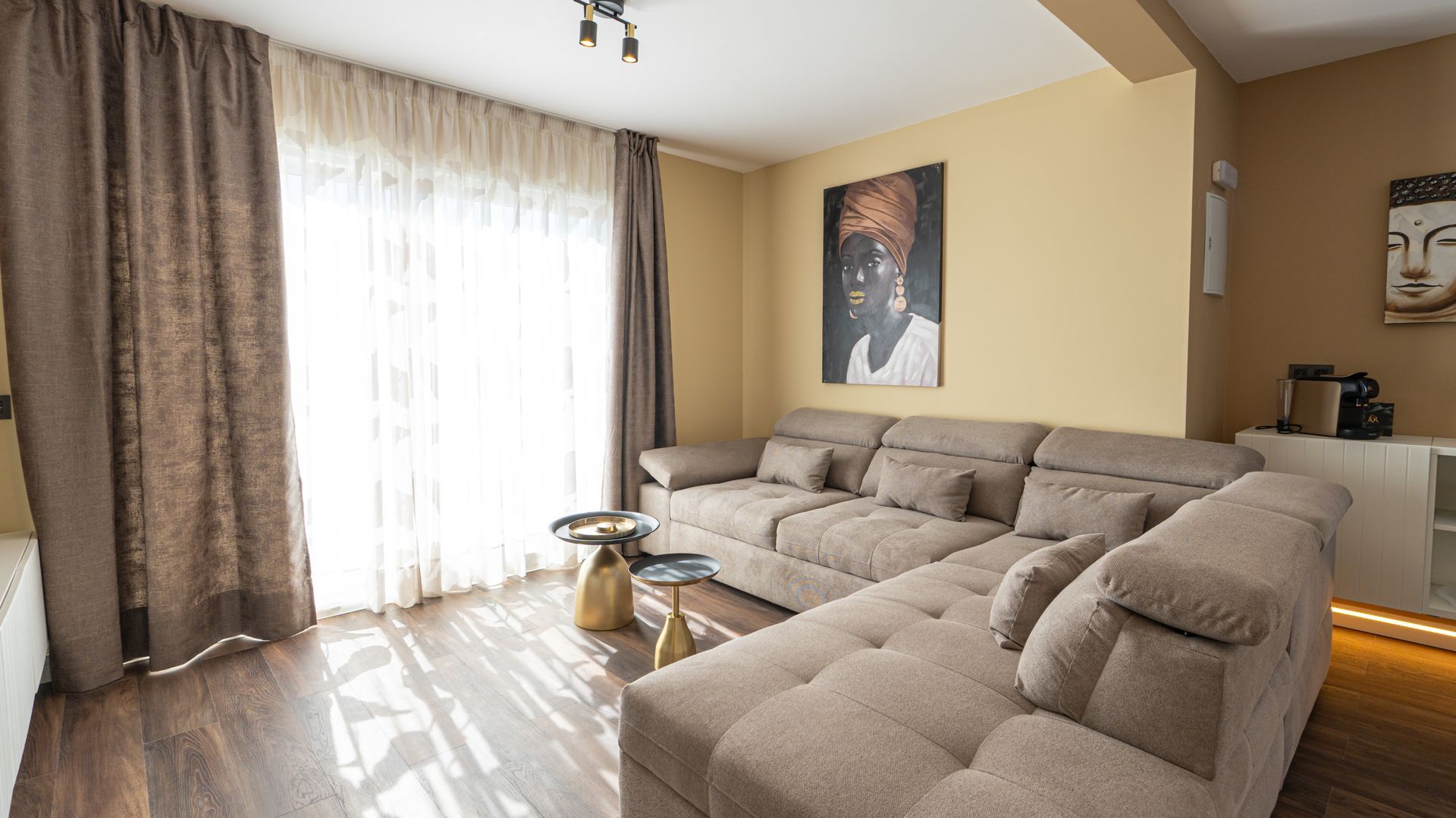 Bright living room with a large beige sectional sofa, sheer curtains, wall art, and sunlight on the floor