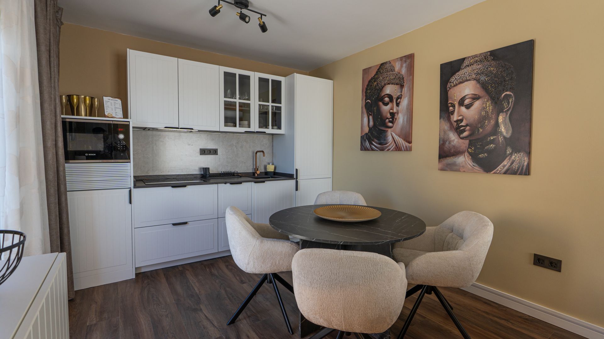 Modern kitchen and dining nook with white cabinets, round table, beige chairs, and two wall portraits