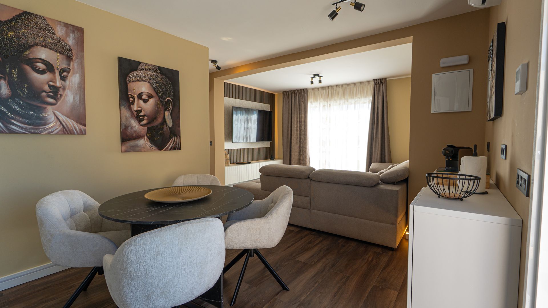 Modern living-dining room with gray sofa, round table, artwork, and large window with curtains