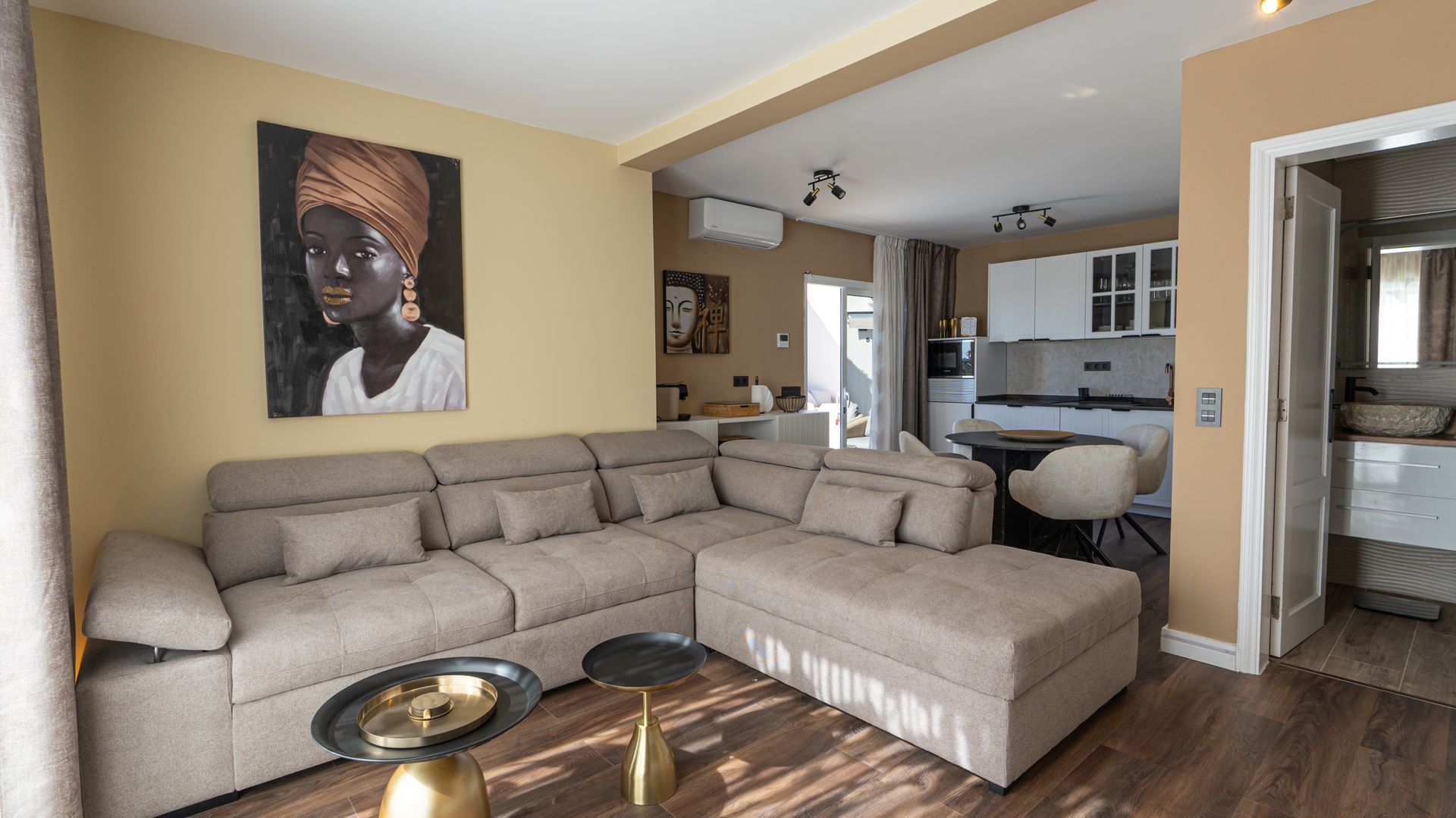 Modern living room with beige sectional sofa, wall art, and an open view into a kitchen