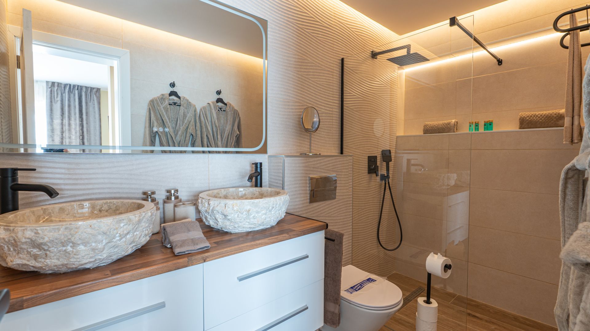 Modern bathroom with double sink vanity, large mirror, walk-in shower, and warm lighting
