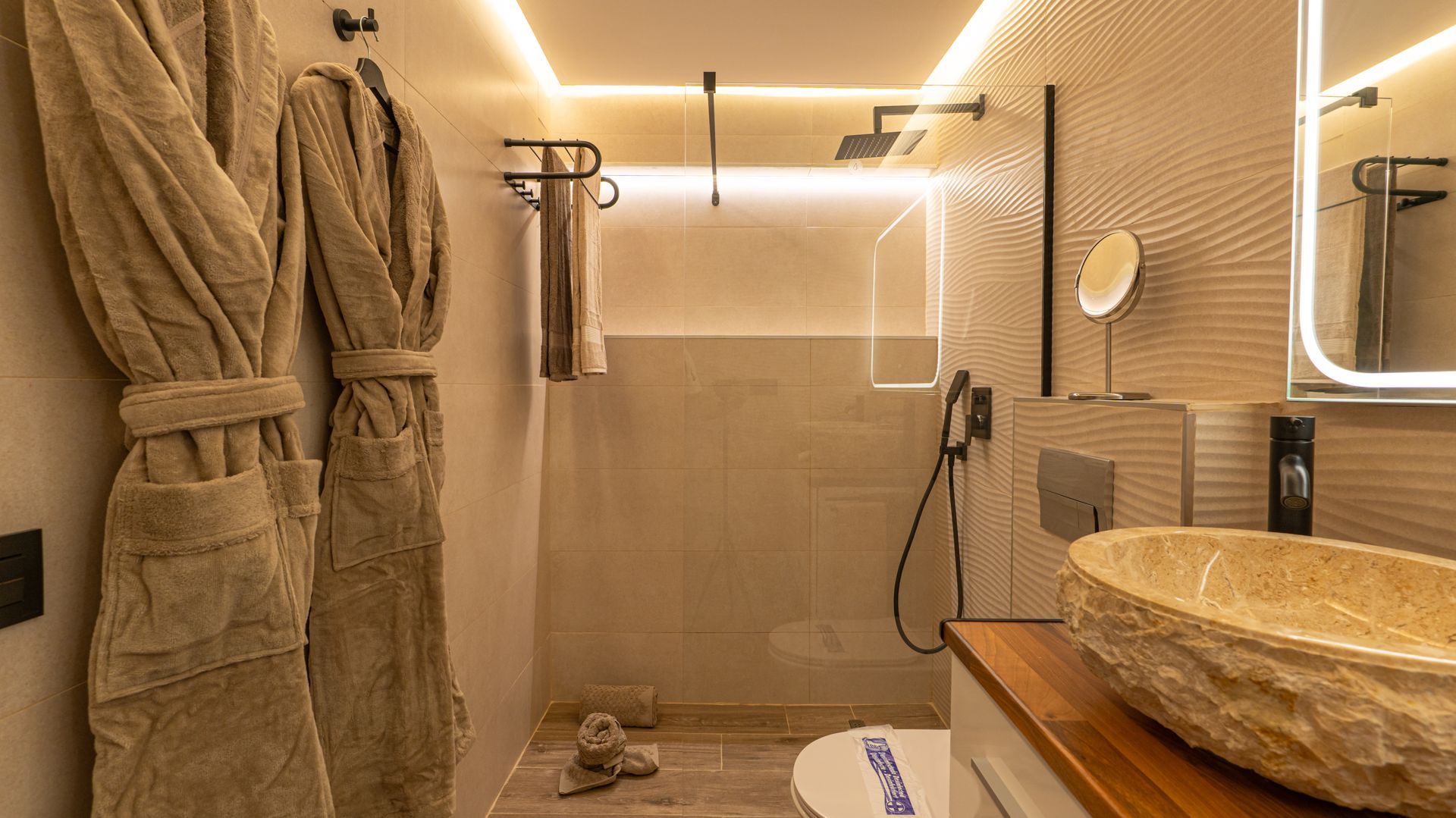 Modern beige bathroom with walk-in shower, towels, sink, and warm lighting