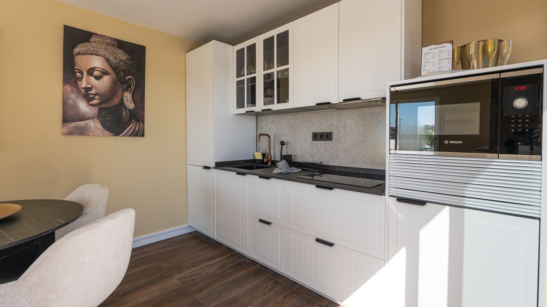 Compact modern kitchen with white cabinets, black countertops, wood floor, and a Buddha wall art print