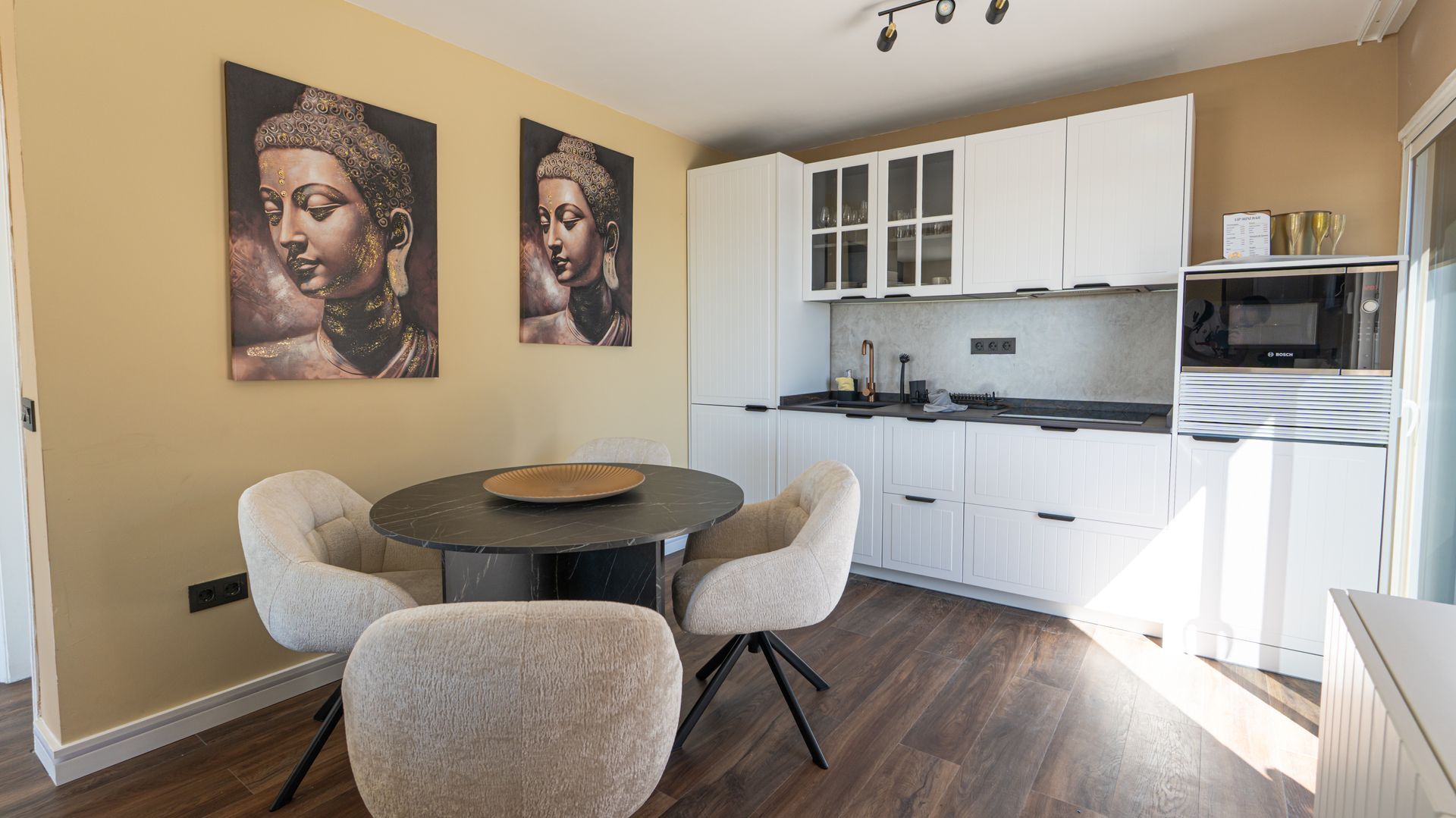 Modern dining nook with round table, plush chairs, wall art, and white kitchen cabinets