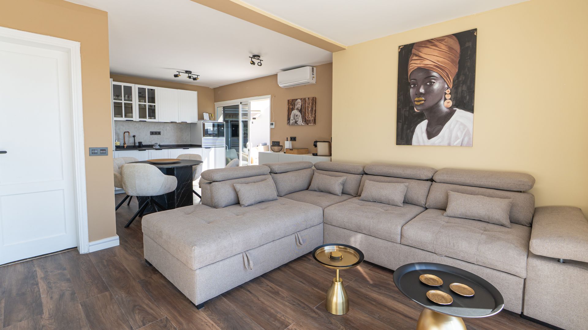 Bright living room with a beige sectional sofa, gold coffee tables, and a portrait on the wall.
