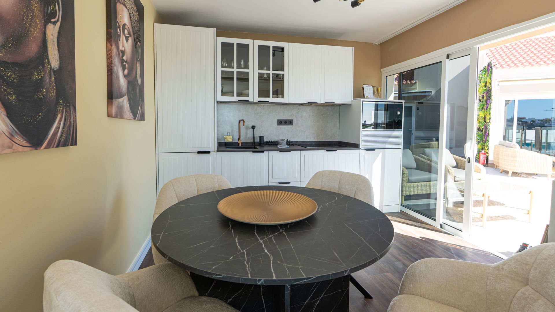 Bright kitchen-dining area with round black table, white cabinets, and open door to a sunny patio.