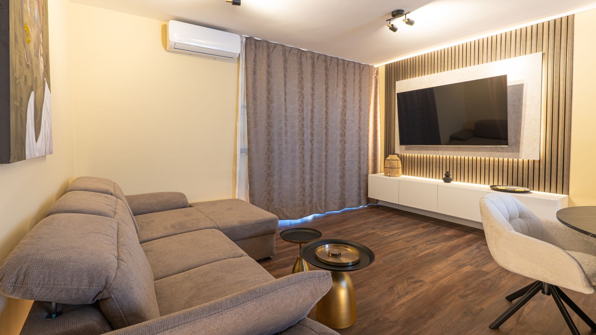 Modern living room with gray sectional sofa, wall-mounted TV, white chair, and warm lighting