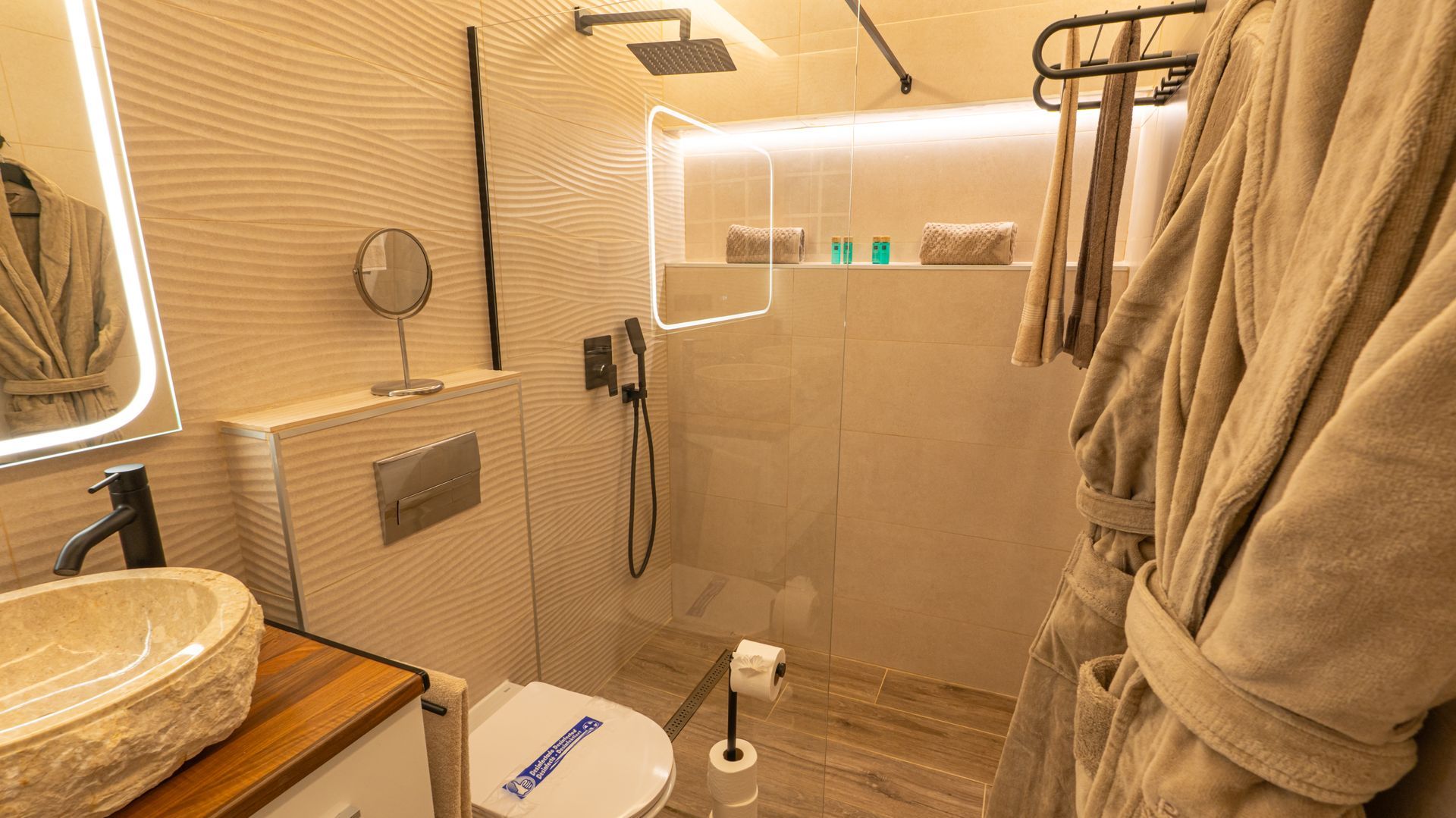 Modern beige bathroom with glass shower, sink, toilet, and towel hanging on the right.