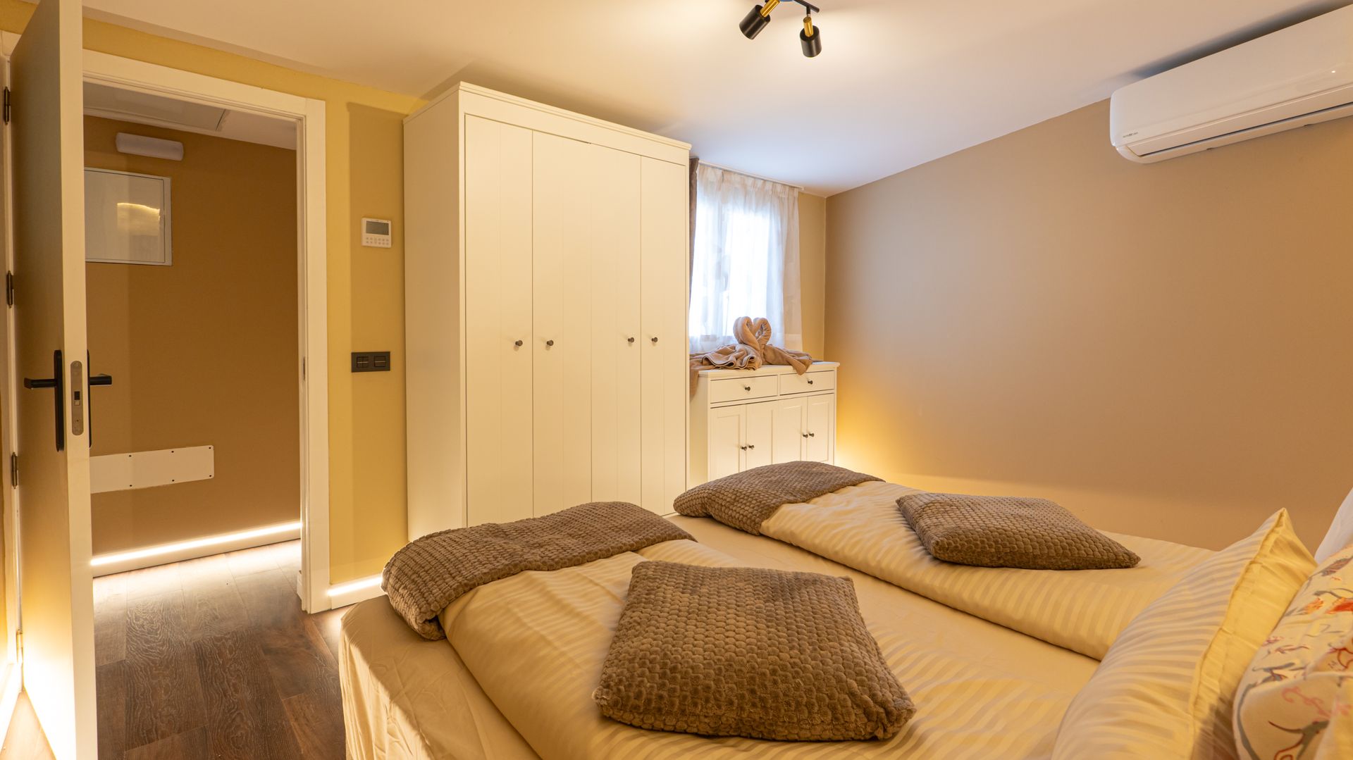 Bright bedroom with a double bed, white wardrobe, dresser, and warm beige walls
