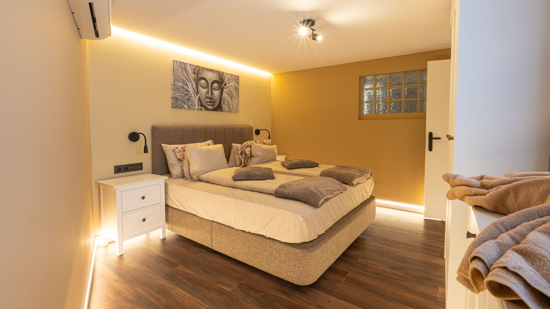 Modern bedroom with beige walls, white bedding, wood floor, and soft warm lighting