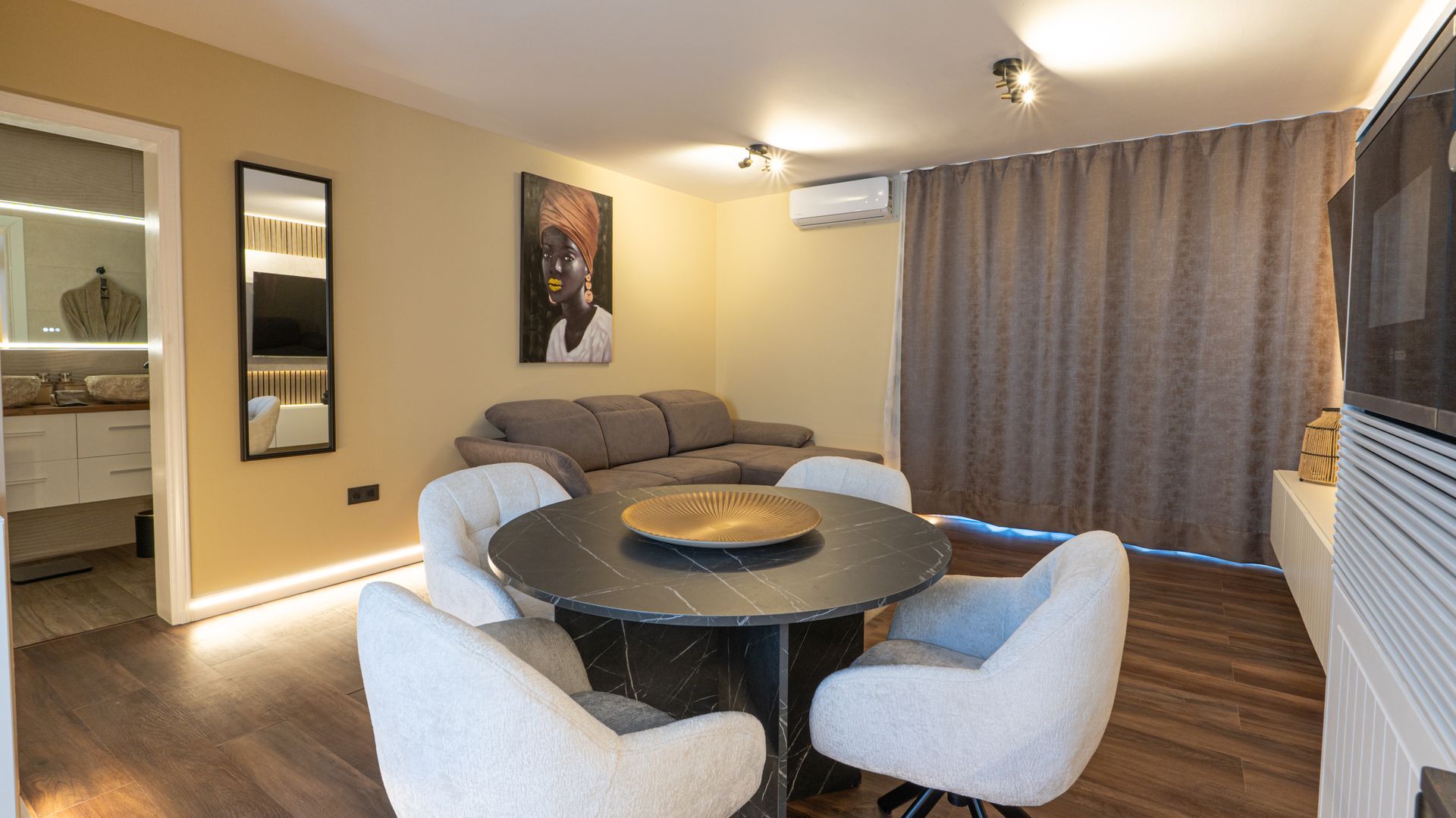 Modern living room with gray sofa, round table, four chairs, wall art, and curtains