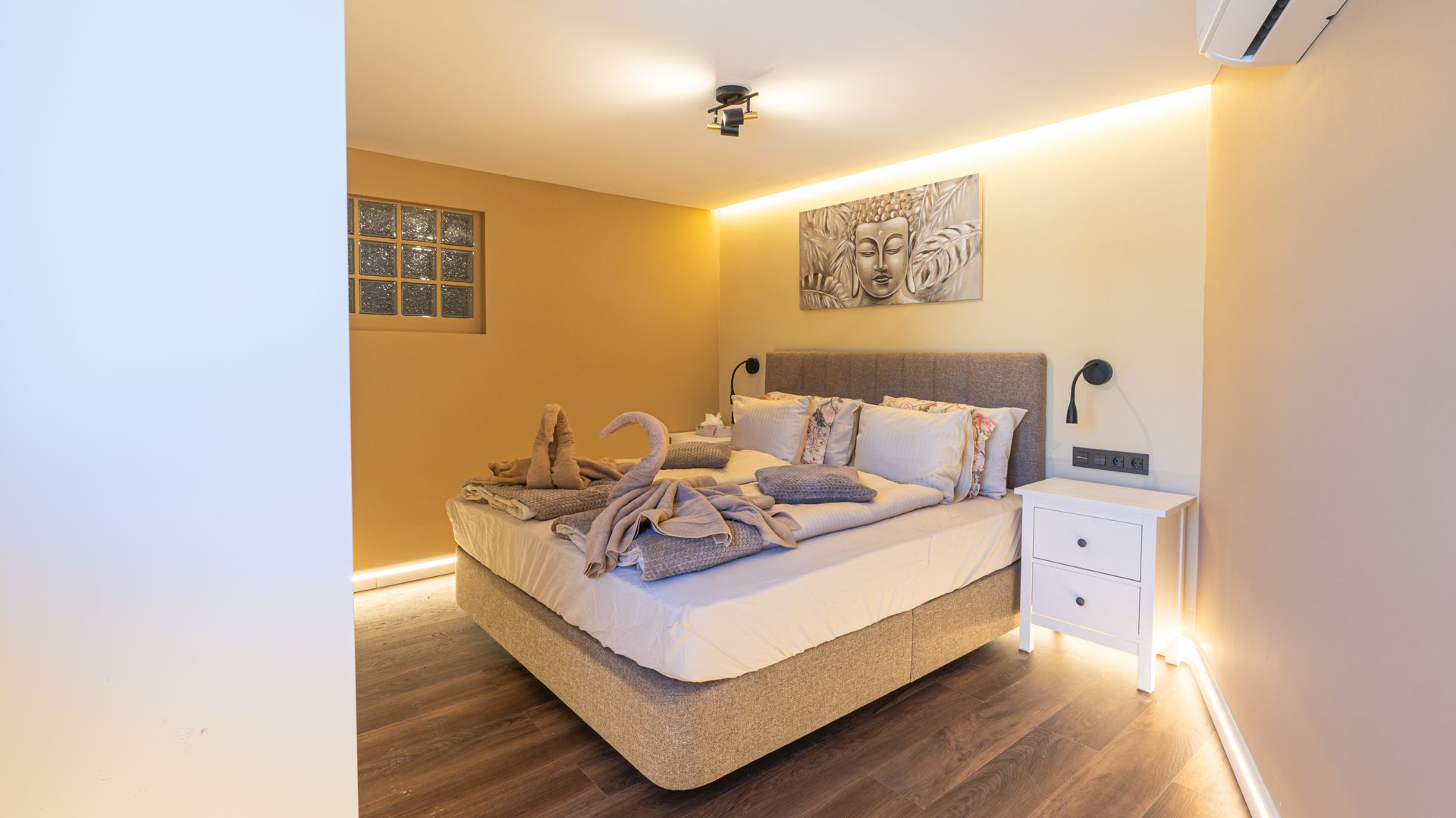 Cozy modern bedroom with a neatly made bed, warm lighting, wood floor, and bedside tables
