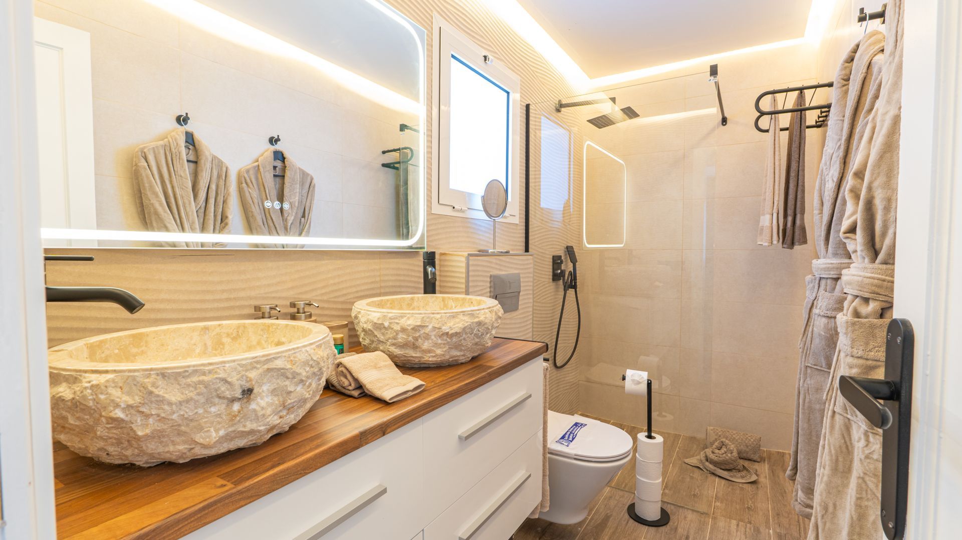 Bright modern bathroom with stone sinks, vanity, shower, and soft warm lighting