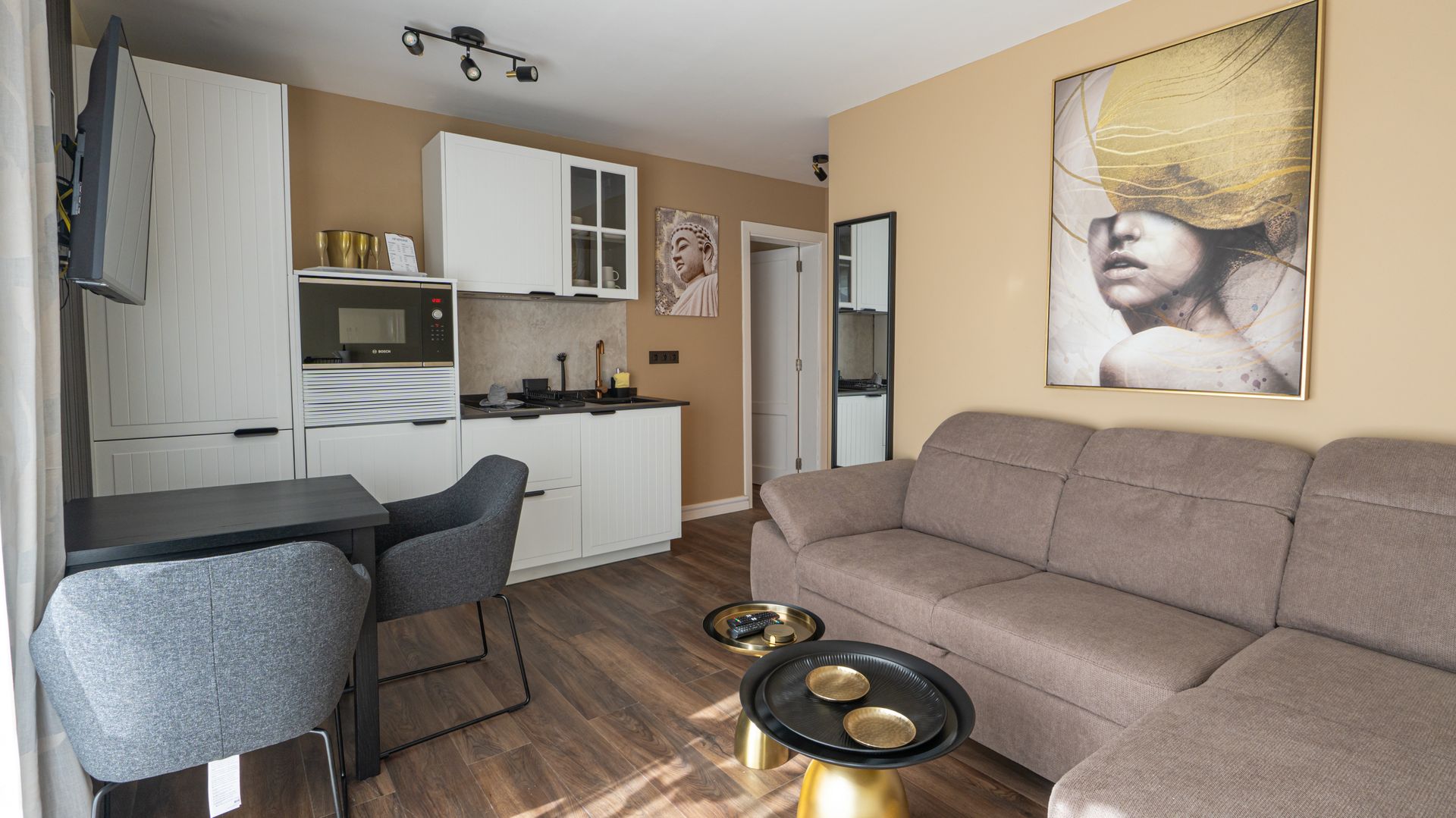 Modern studio apartment with gray sofa, kitchenette, small dining table, and wall art